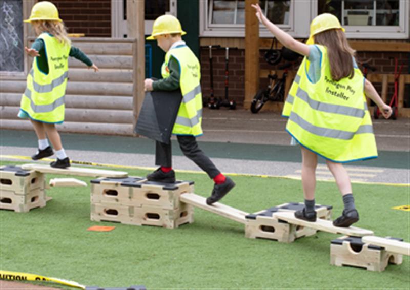 Three children taking it in turns to walk over a trail made from Play Builder blocks